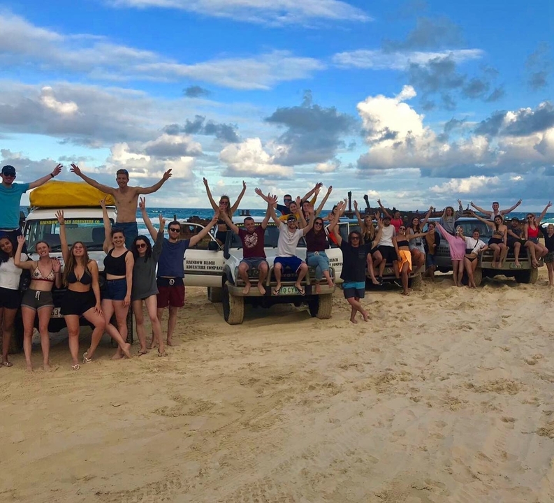 A large group of people posing with vehicles on a beach.