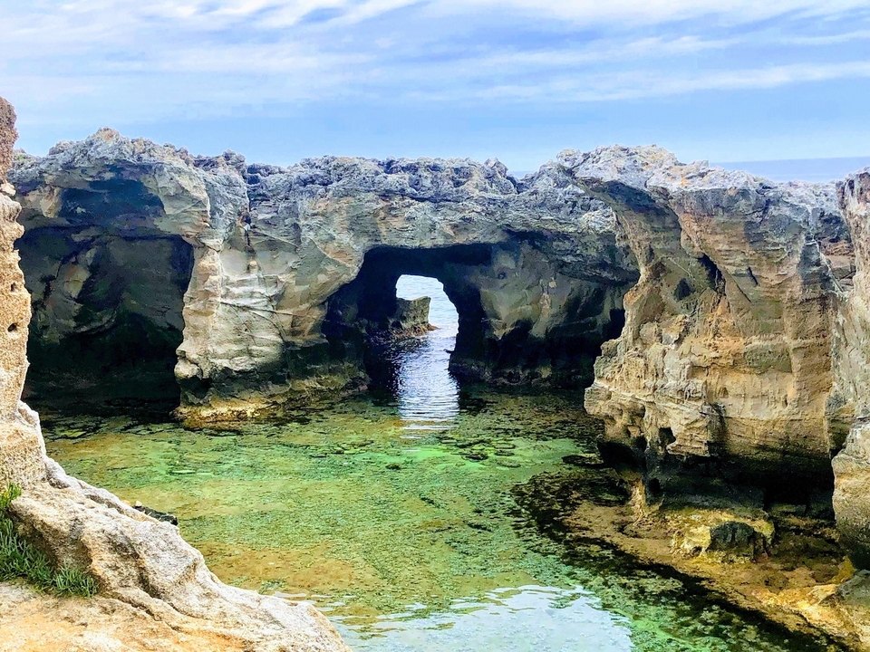 Rocky formations with natural arches over clear water.