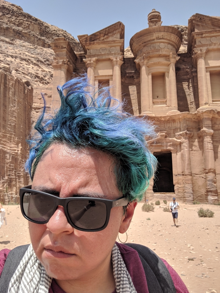 Person with colorful hair standing in front of an ancient structure.