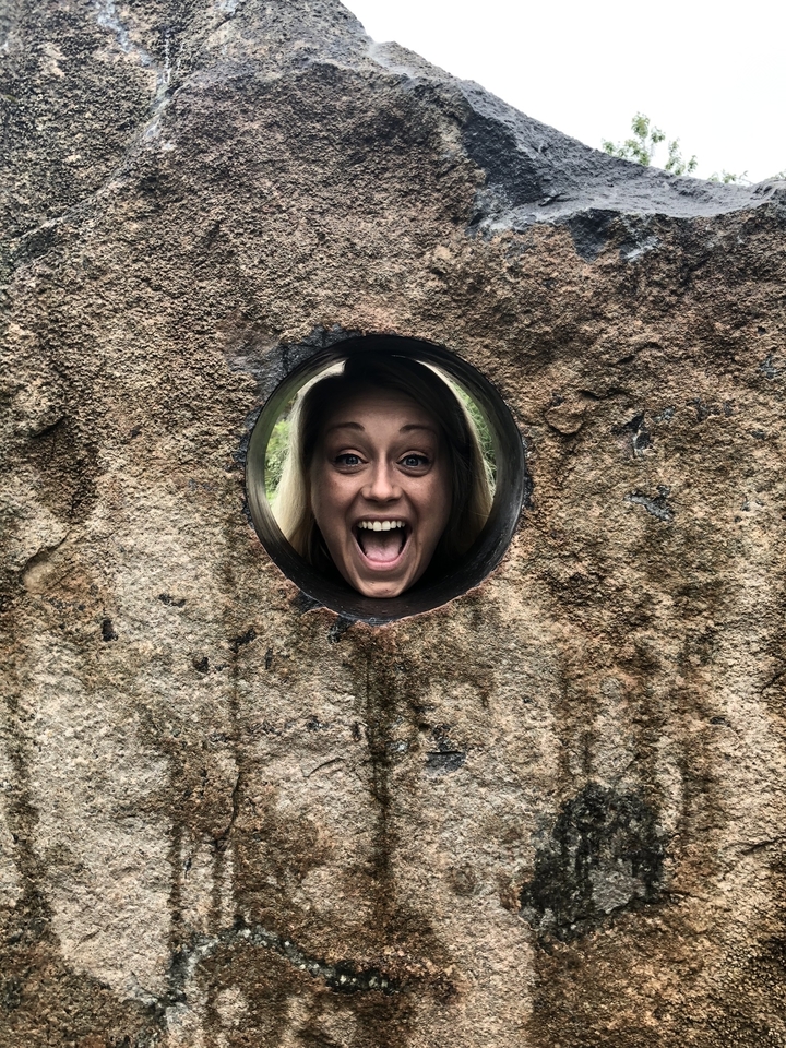 Femme posant de manière ludique derrière une ouverture circulaire dans une pierre.