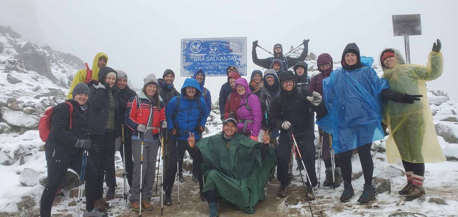 Group posing at Abra Salkantay trek sign in snowy conditions.