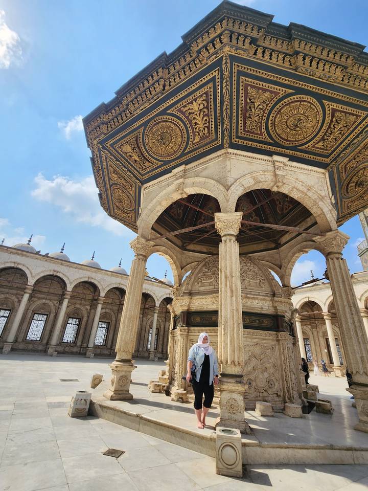 Person posing in front of a large, ornate structure.