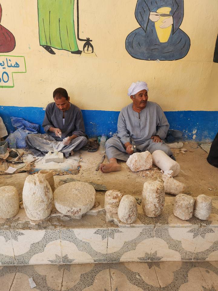 Two men sitting on the ground working with stone carving tools.