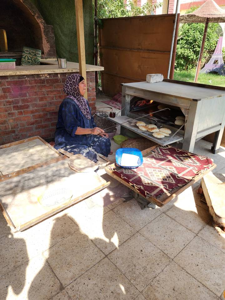 Woman making bread at an outdoor oven.