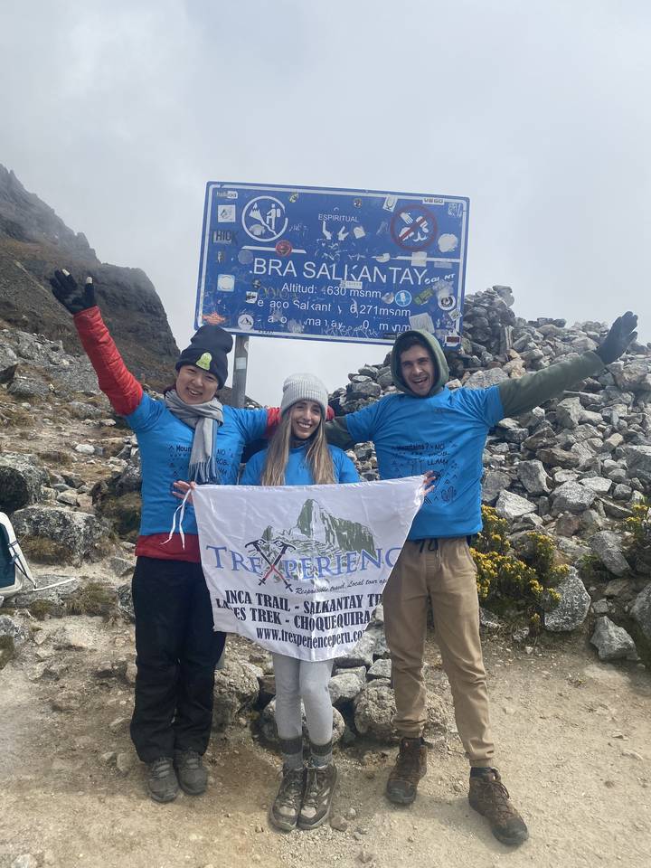 Three people posing with a Salkantay sign; cloudy sky.