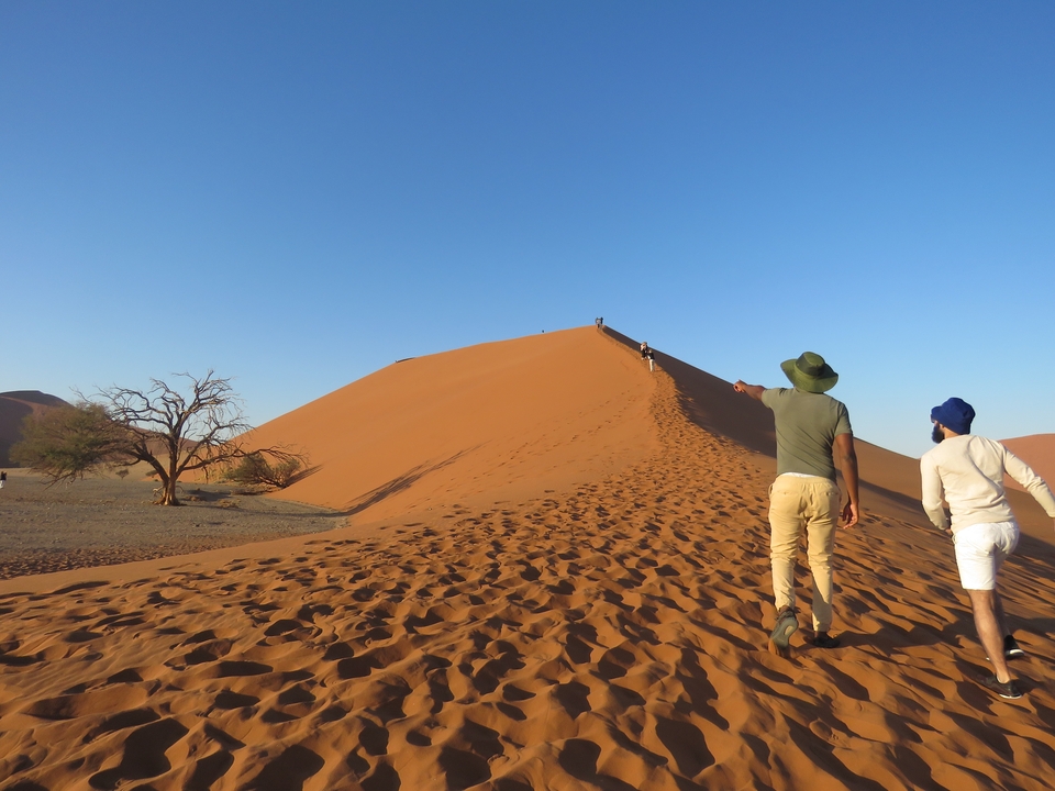 People walking towards a large sand dune.