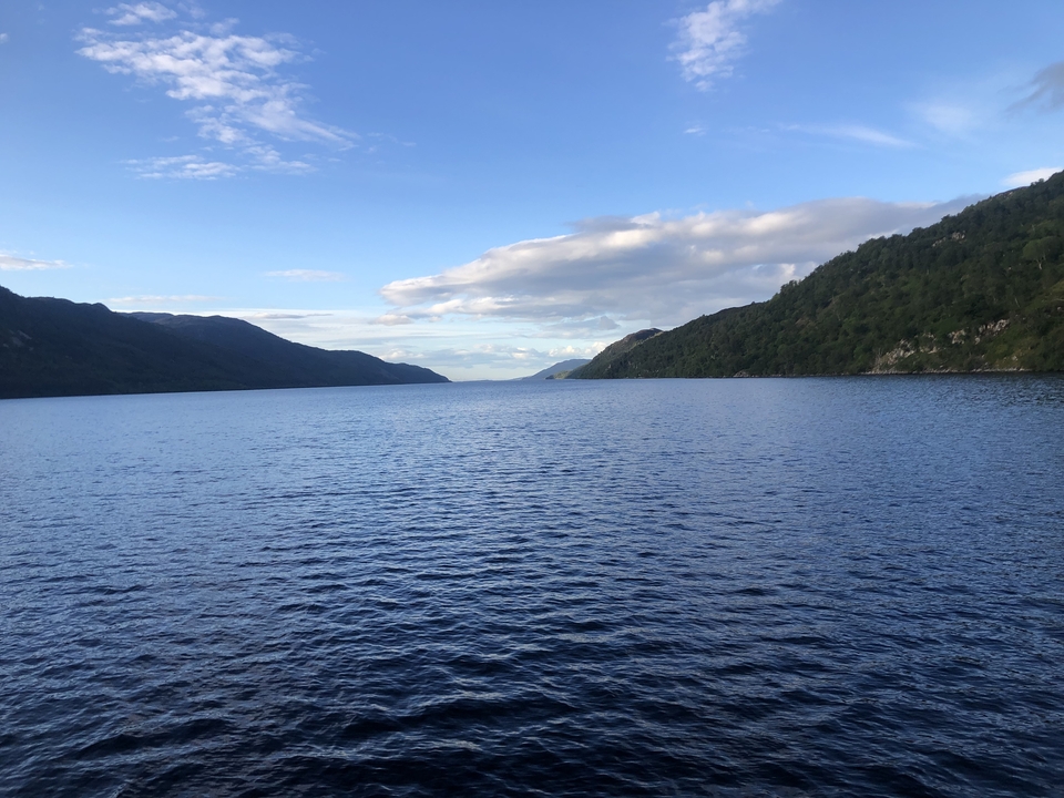 A peaceful lake with surrounding hills under a blue sky.