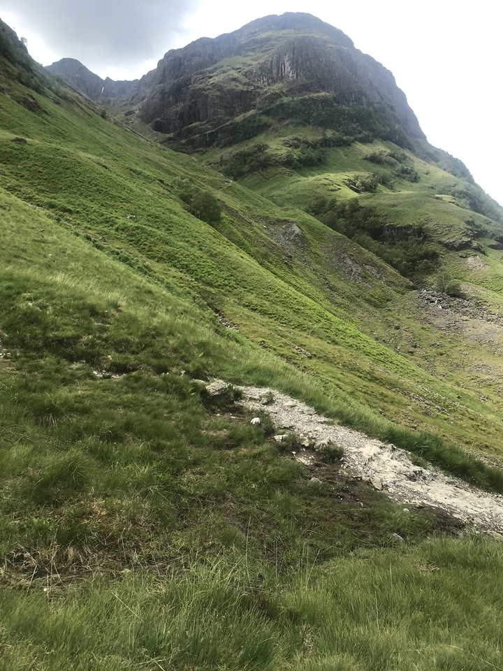 A scenic grass-covered hillside with a steep, rocky slope.