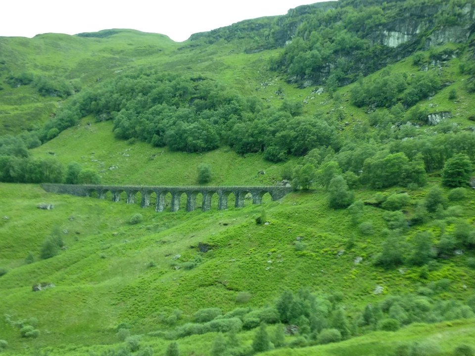 Stone viaduct running through green hills.