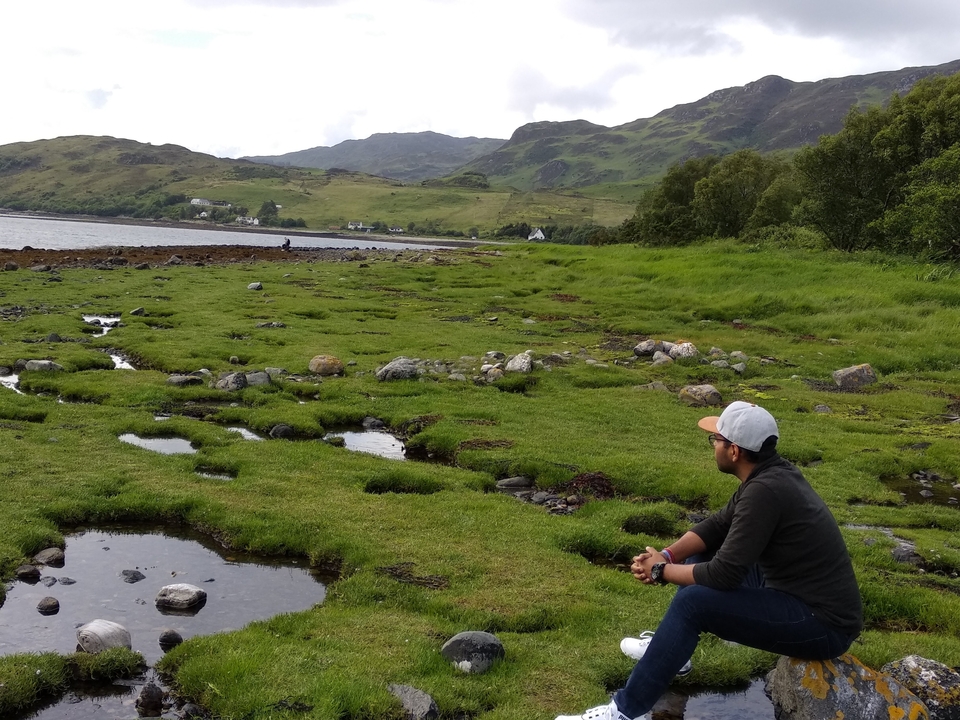 Person sitting on a grassy area near a lake.