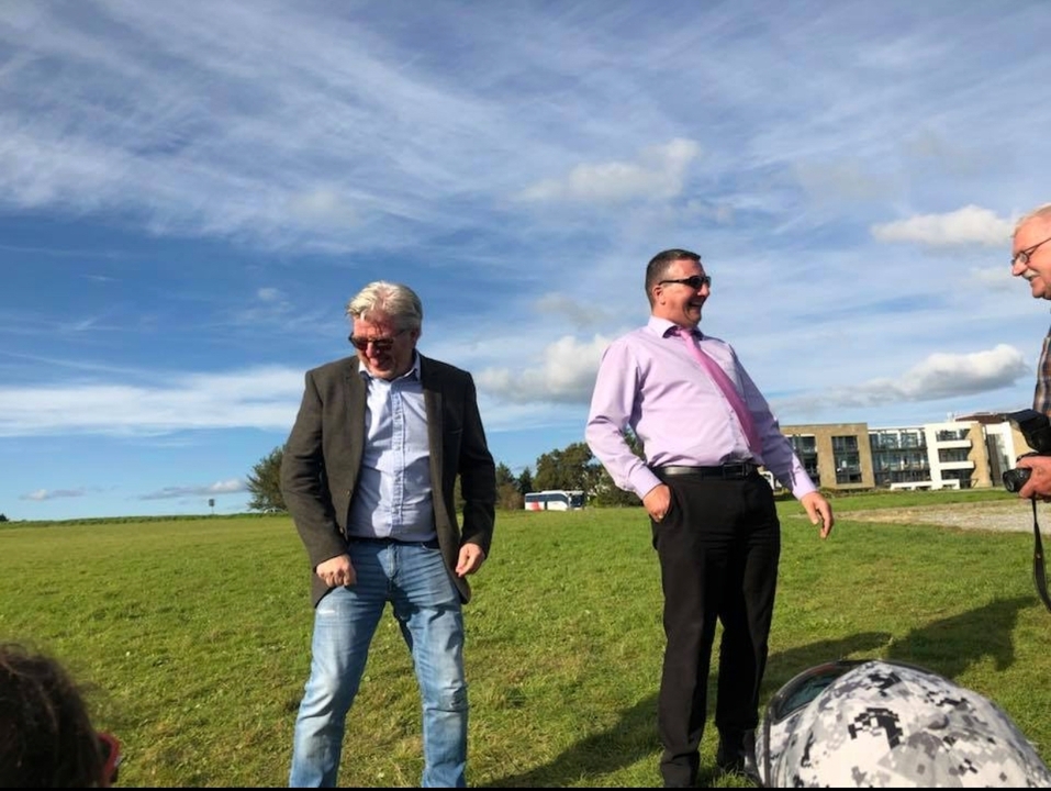 Three men smiling and chatting outdoors on a sunny day.