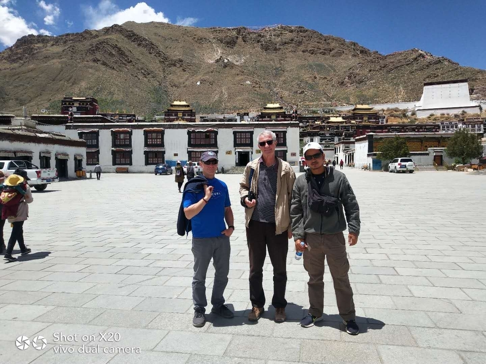 Trois personnes debout dans une grande cour avec des bâtiments traditionnels autour.