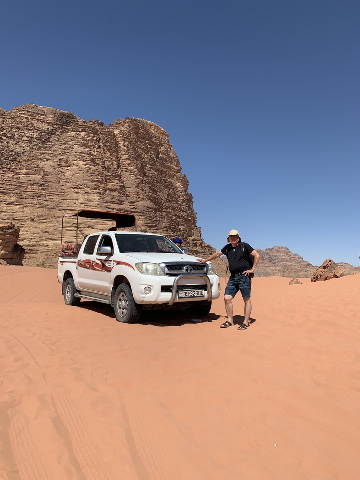 Man posing next to a pickup truck in a desert landscape.