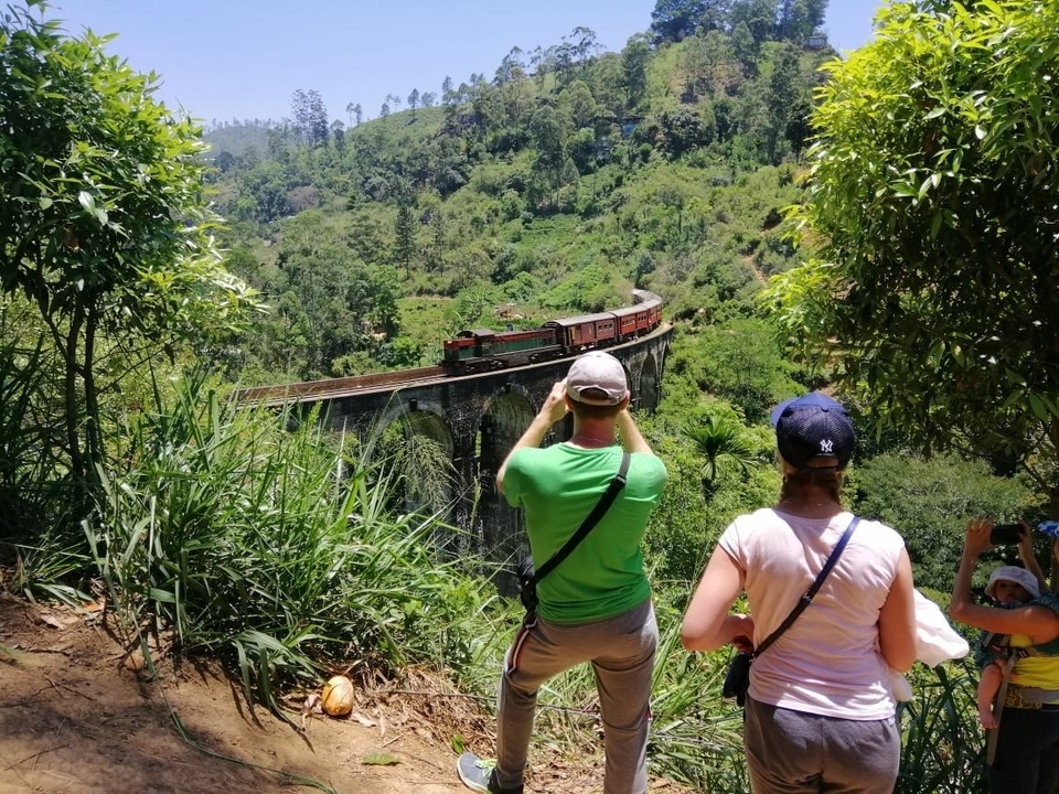 Des gens qui prennent des photos d'un train traversant le pont à neuf arches.