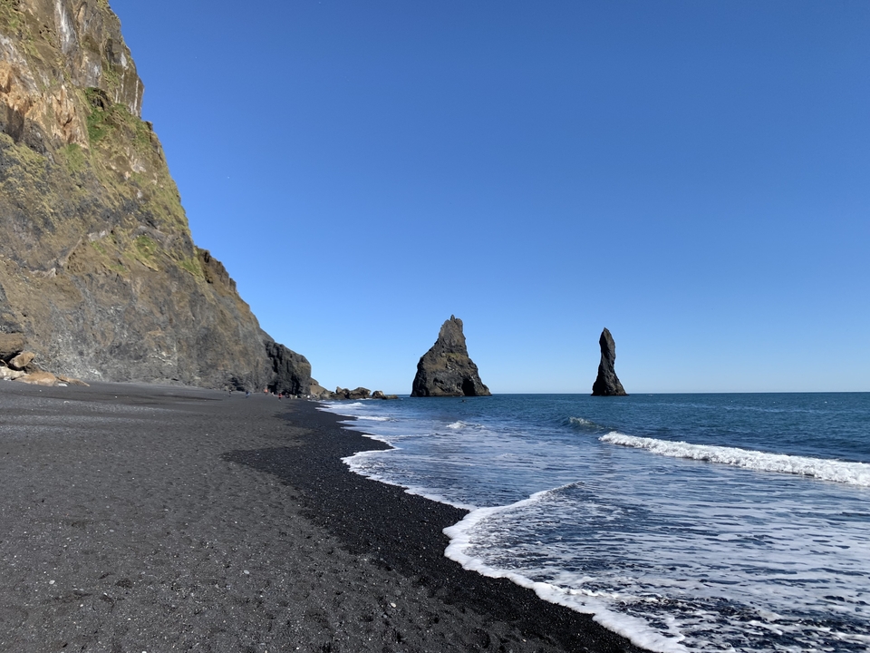 Black sand beach with basalt sea stacks and cliffs on a clear day.