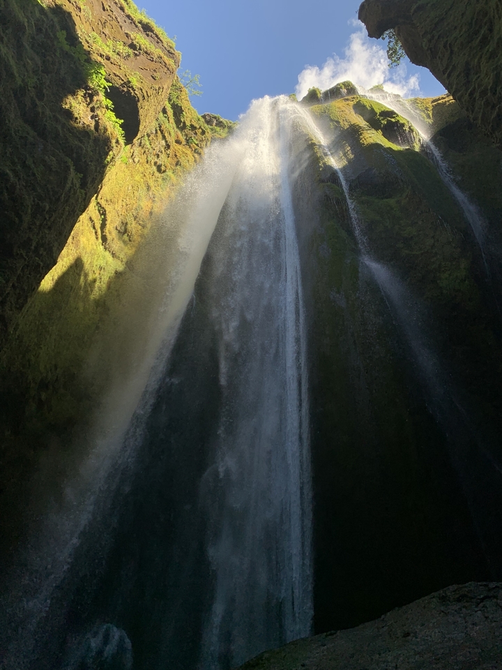 Waterfall inside a dark cave with light filtering in.
