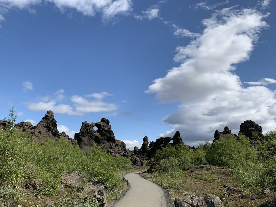 Unique lava formations with green and rocky terrain under a cloudy sky.