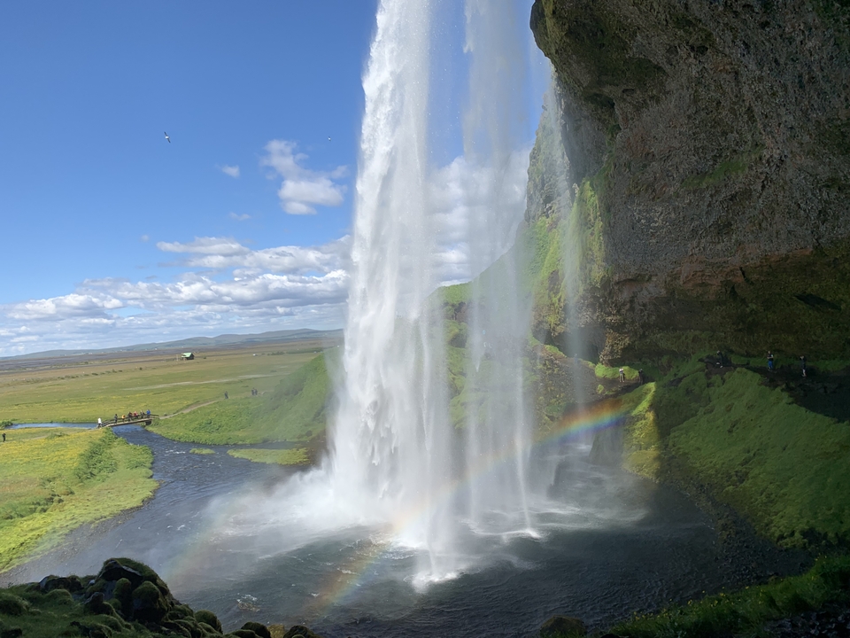Waterfall with a visible rainbow and lush green landscape.