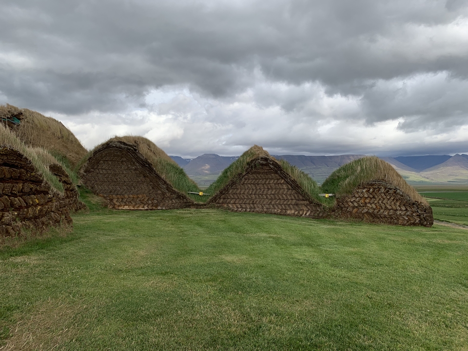 Traditional turf houses against a mountainous background under a cloudy sky.