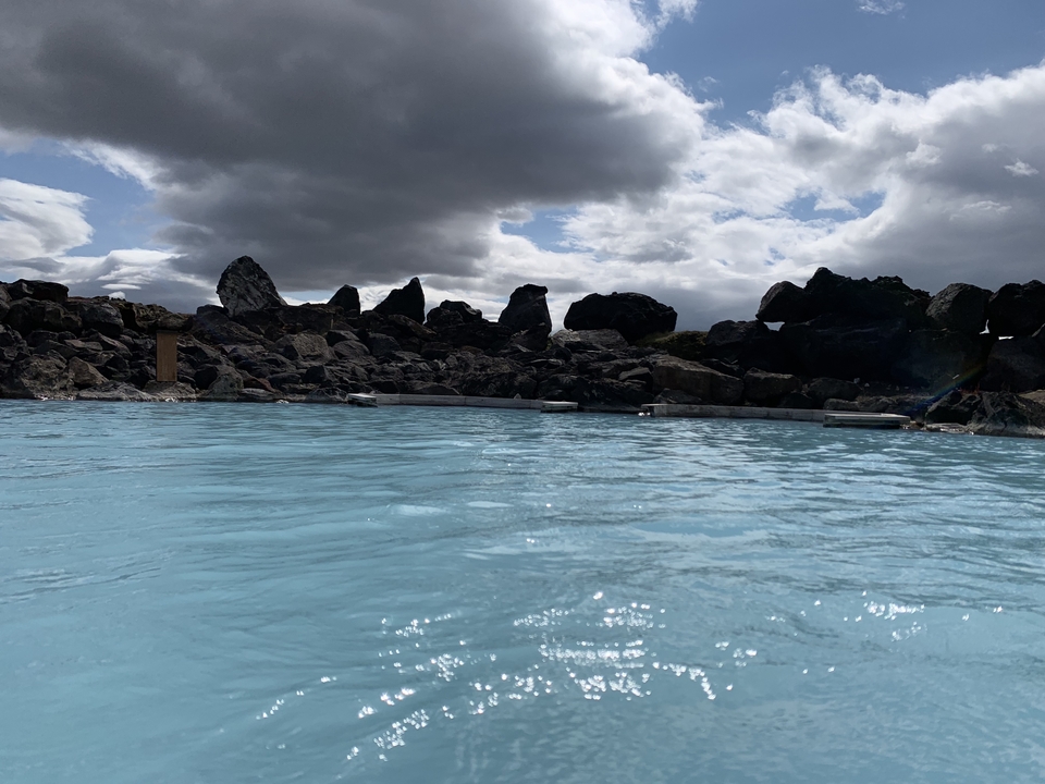 Rocky hot spring pool with steam surrounded by lush vegetation and rocky outcroppings.