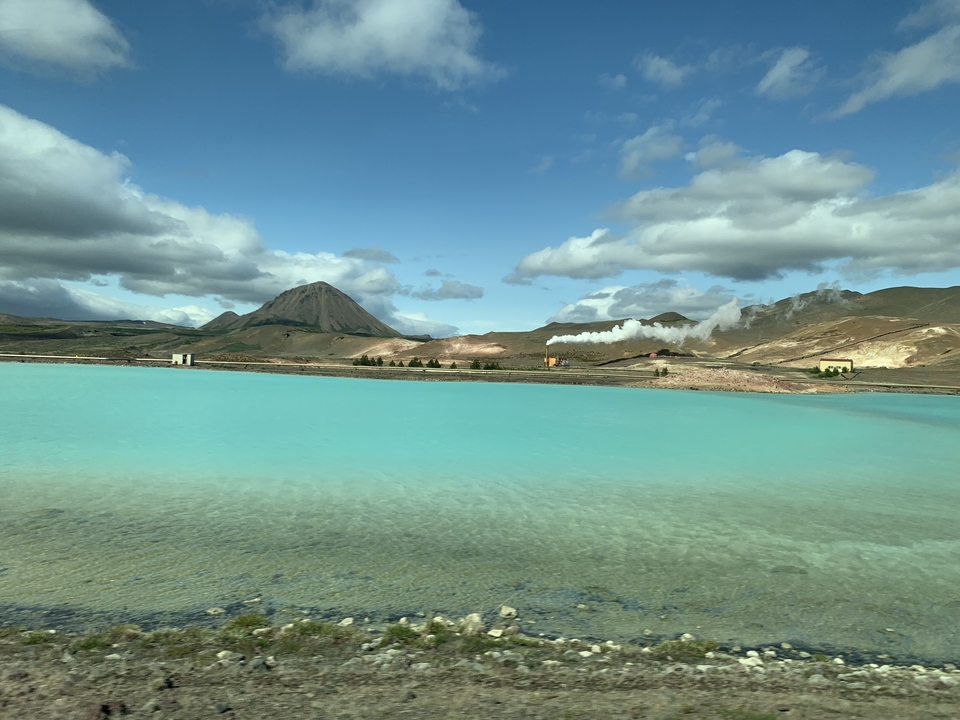 Turquoise geothermal pool with vapor rising and mountains in the distance.