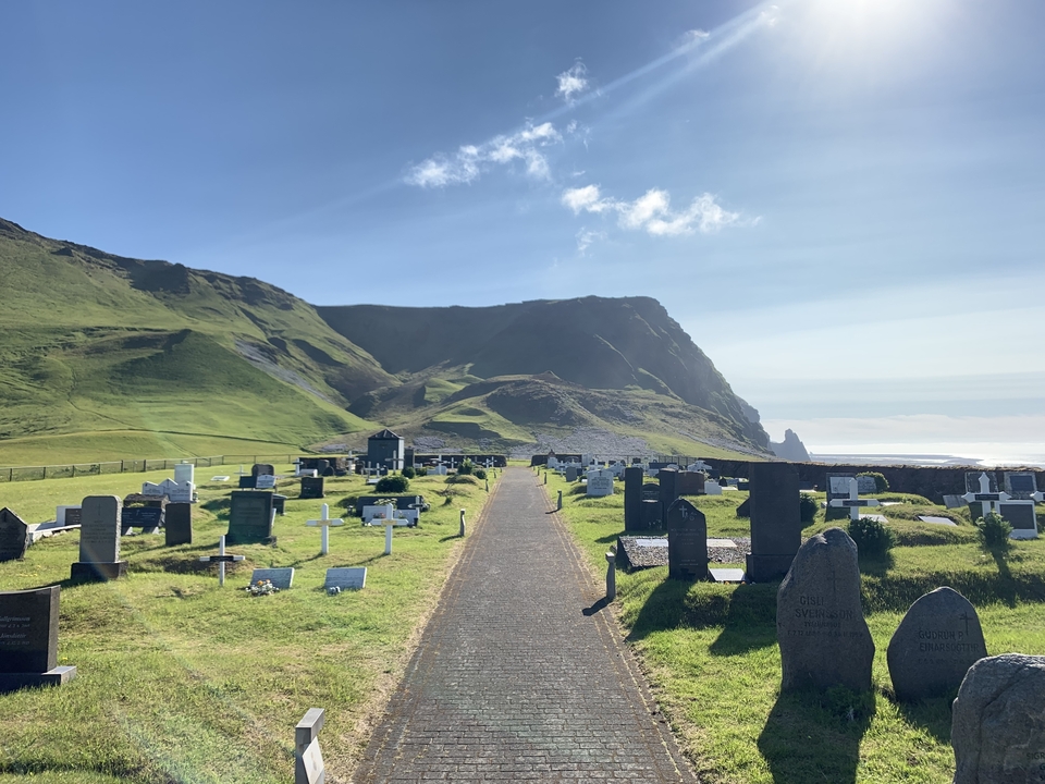 Grassy graveyard with mountain in the background and a path leading through the tombstones.