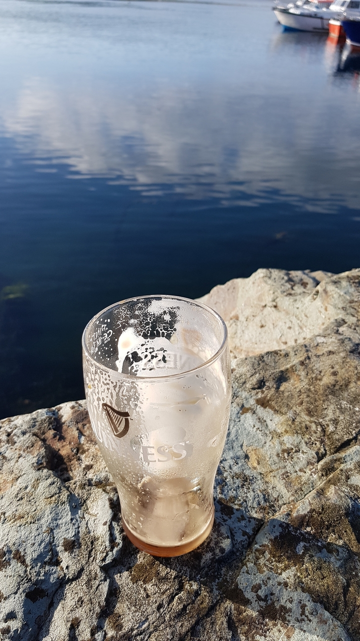 Empty beer glass on a rock with a view of the sea.