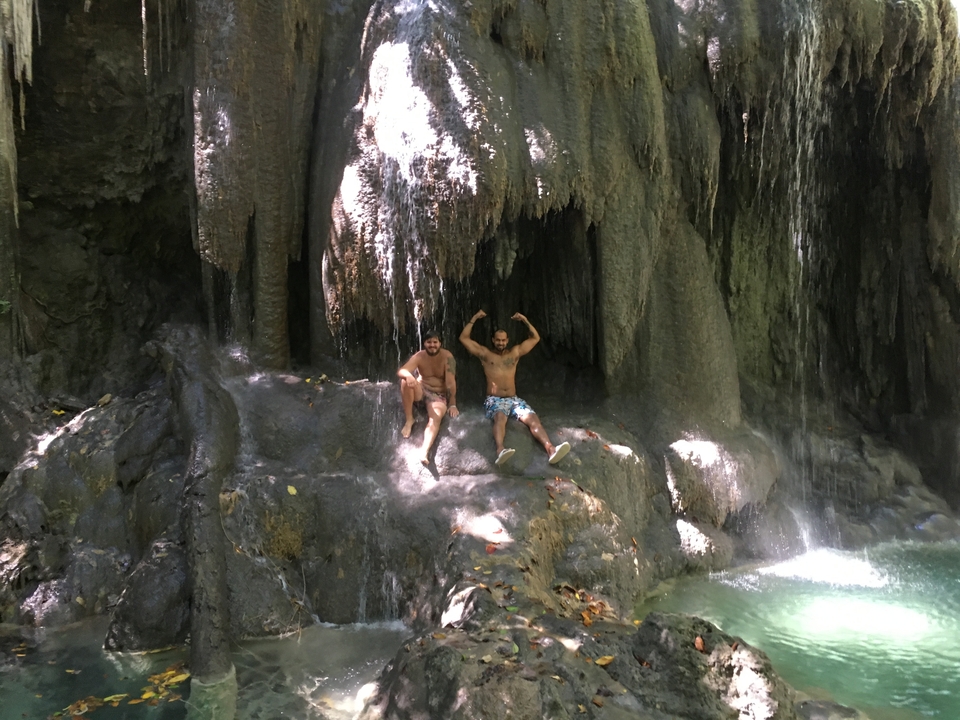 Deux hommes assis sous une cascade en maillot de bain.