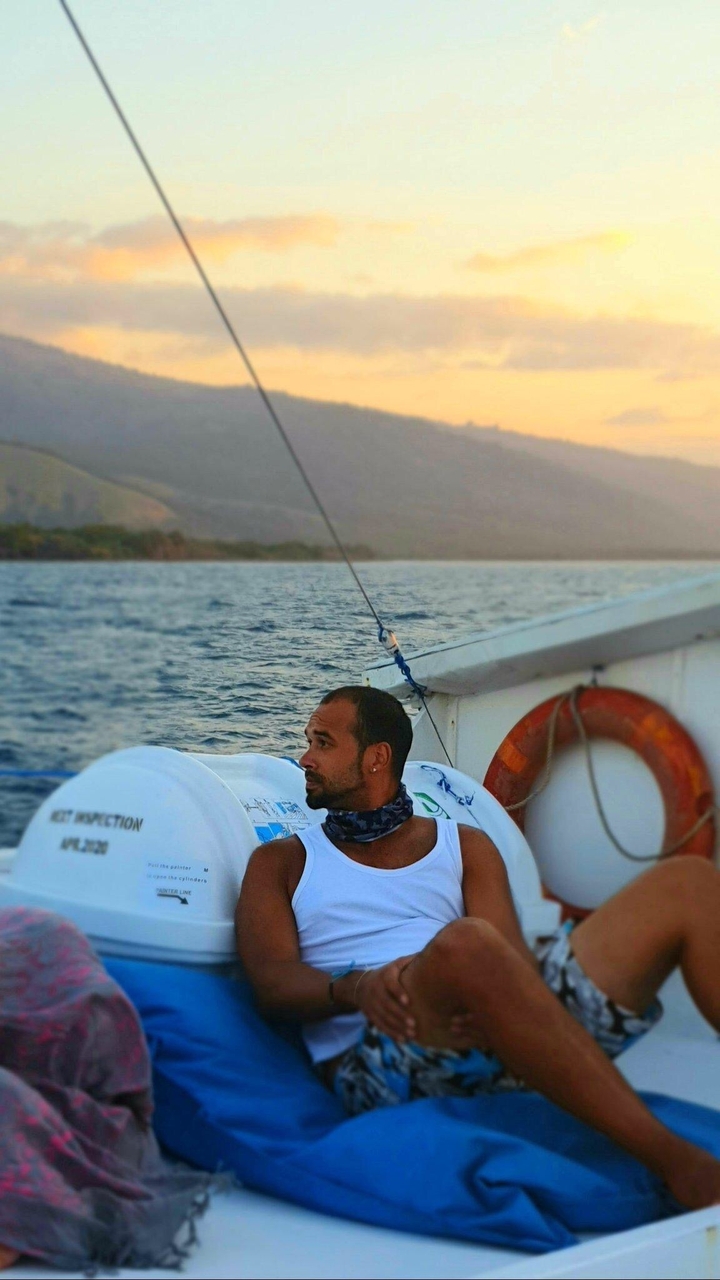 Homme sur un bateau avec la mer et une colline en arrière-plan.
