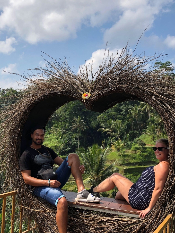 Couple sitting in a heart-shaped structure with greenery in the background.