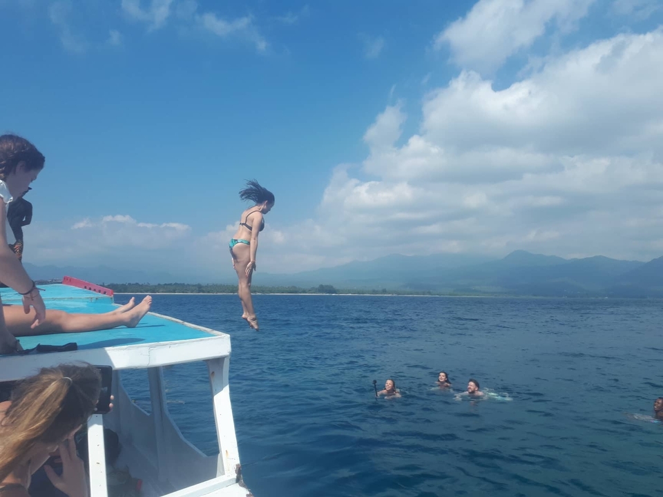 Person jumping off a boat into the sea with others swimming.