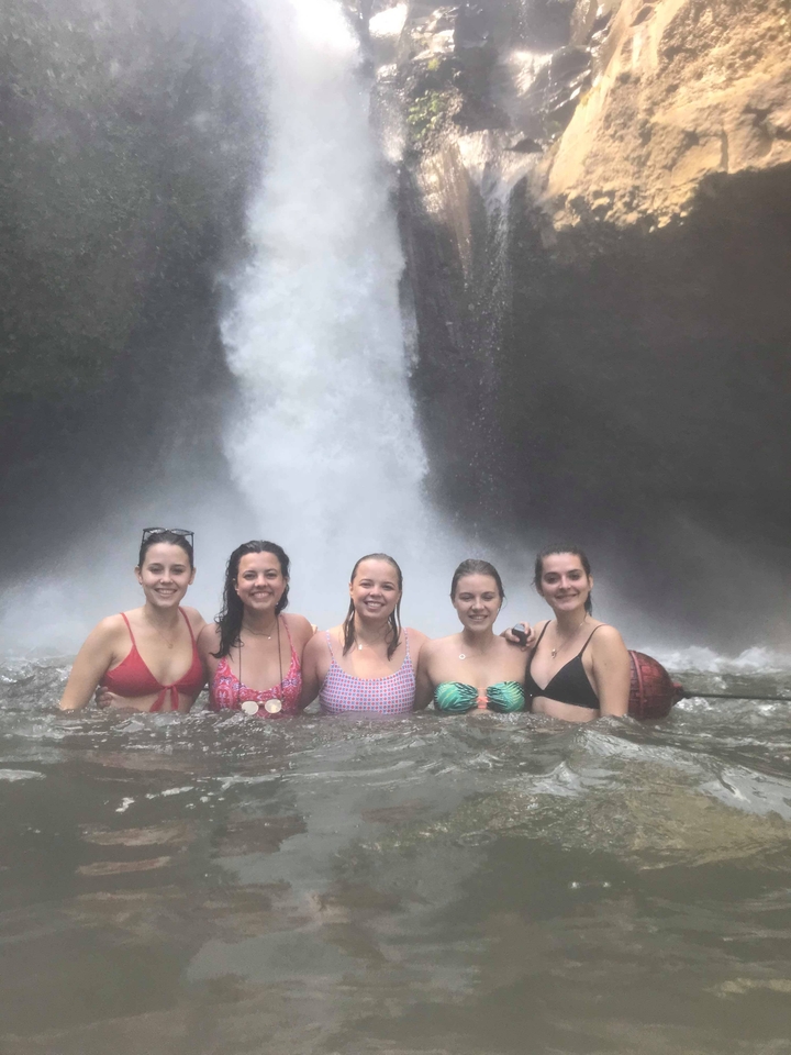 Group of women swimming in front of a waterfall.