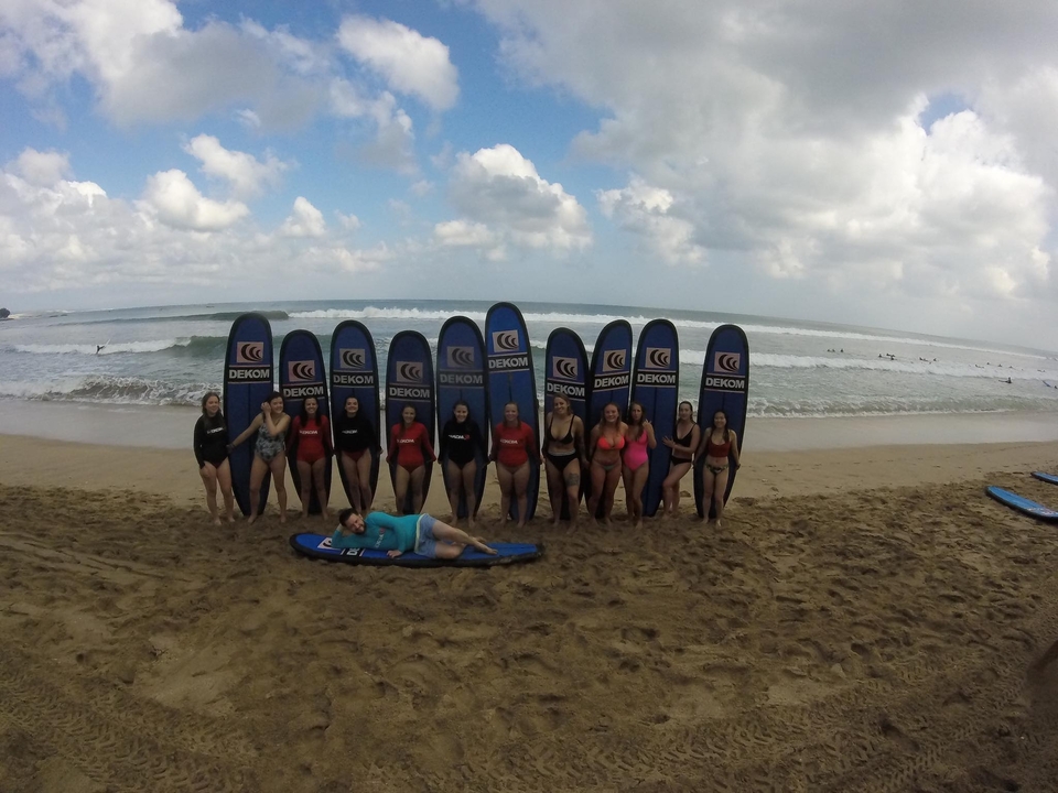 Group of people posing with surfboards on a beach.