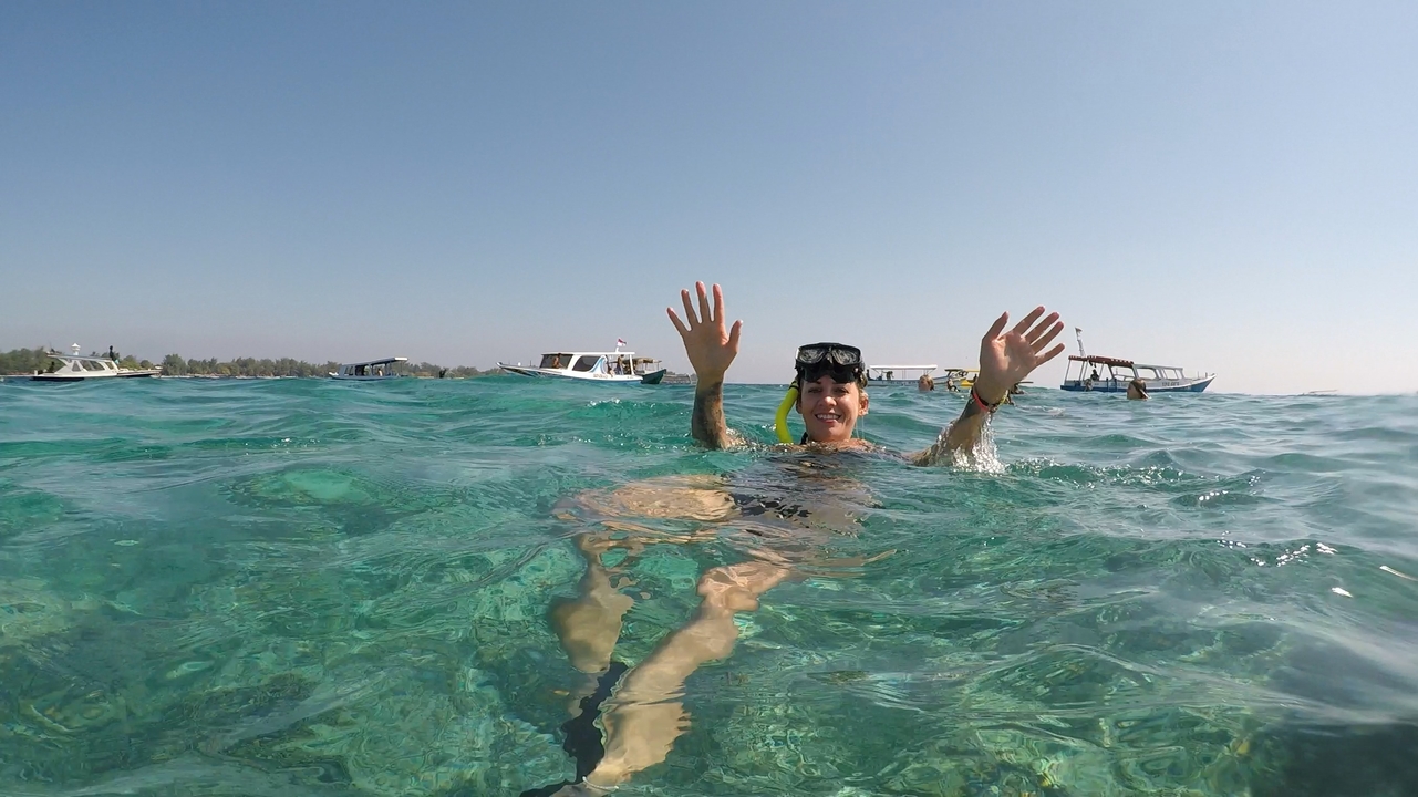 Woman swimming in turquoise waters with boats in the background.