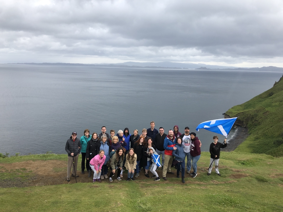 Group holding Scottish flags on a cliff overlooking the sea.