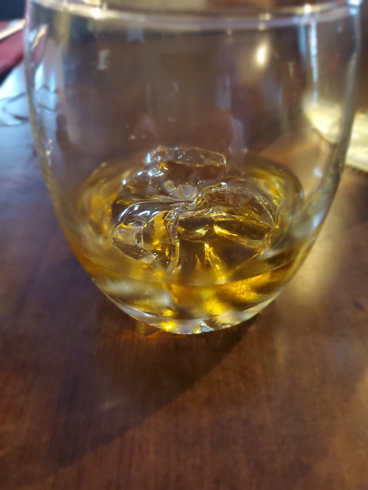 A glass of whiskey with ice on a wooden table.