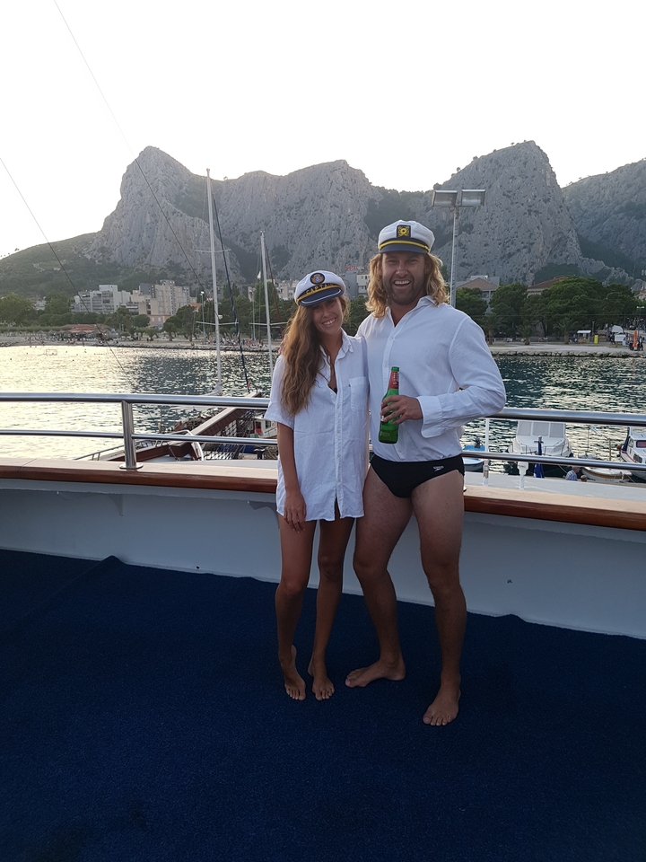 Couple on a boat with a city and mountain backdrop.