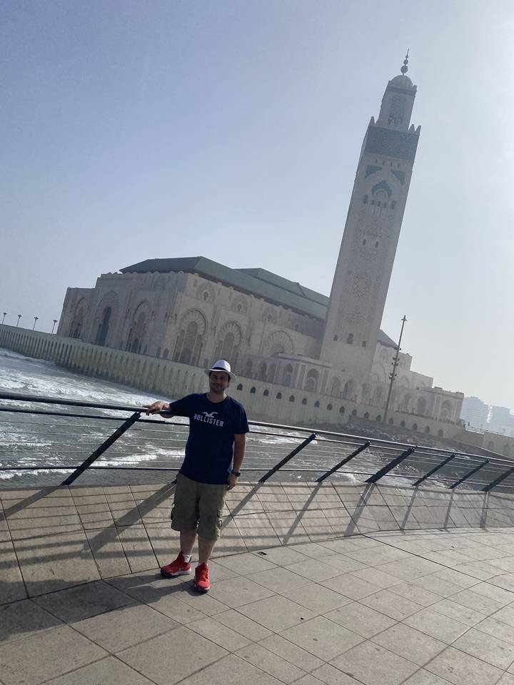 A person posing near a large mosque or building.