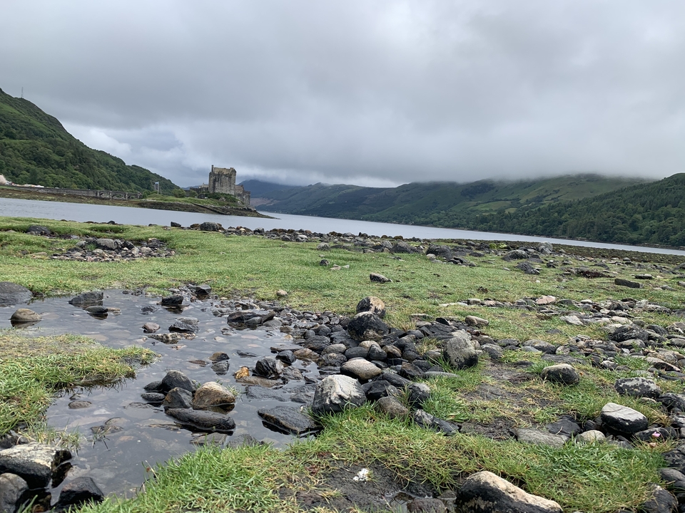 Castle by a lake with rocks and mountains.