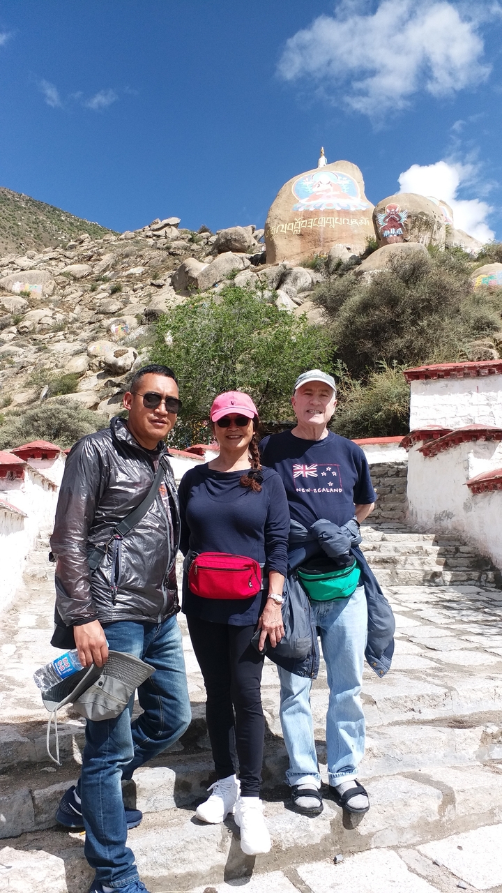 Trois personnes debout à l'extérieur près de marches et d'un paysage rocheux.