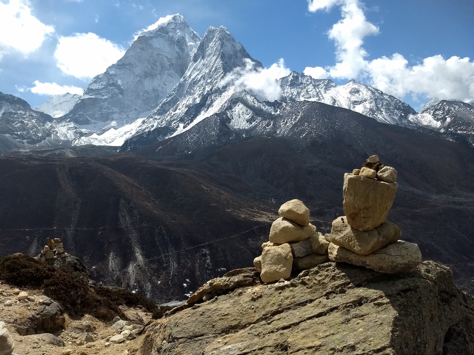 Cairn de pierres sur un sentier de montagne avec des sommets enneigés en arrière-plan.