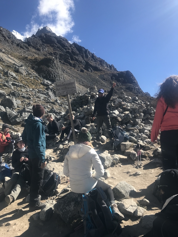 Grupo de personas en un sendero rocoso de montaña con una señal direccional.