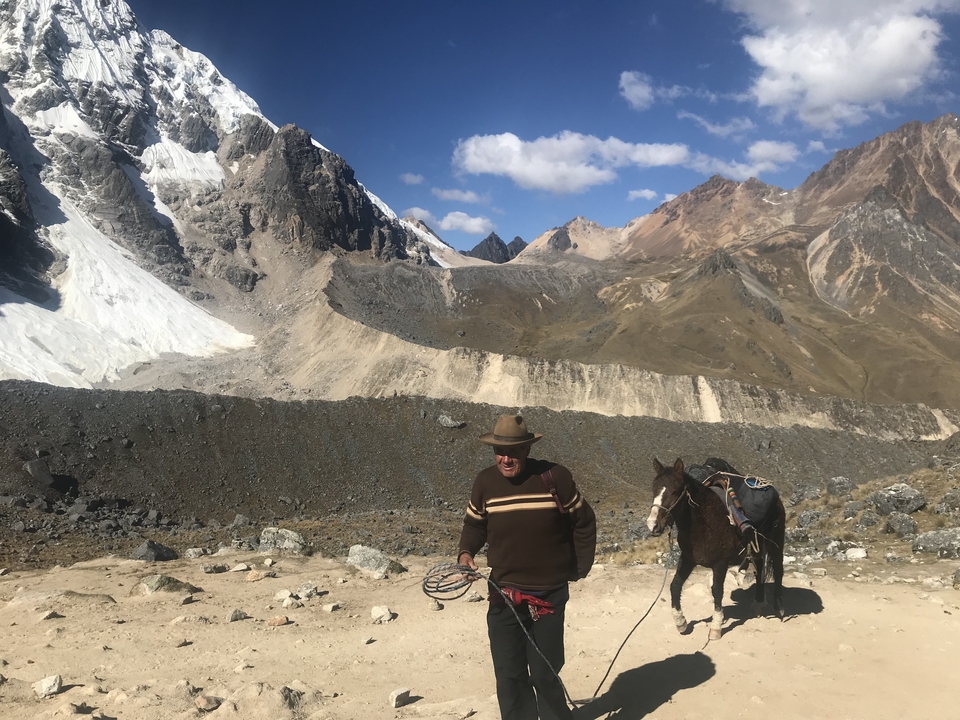 Persona con un caballo en un sendero de montaña con vistas al glaciar.