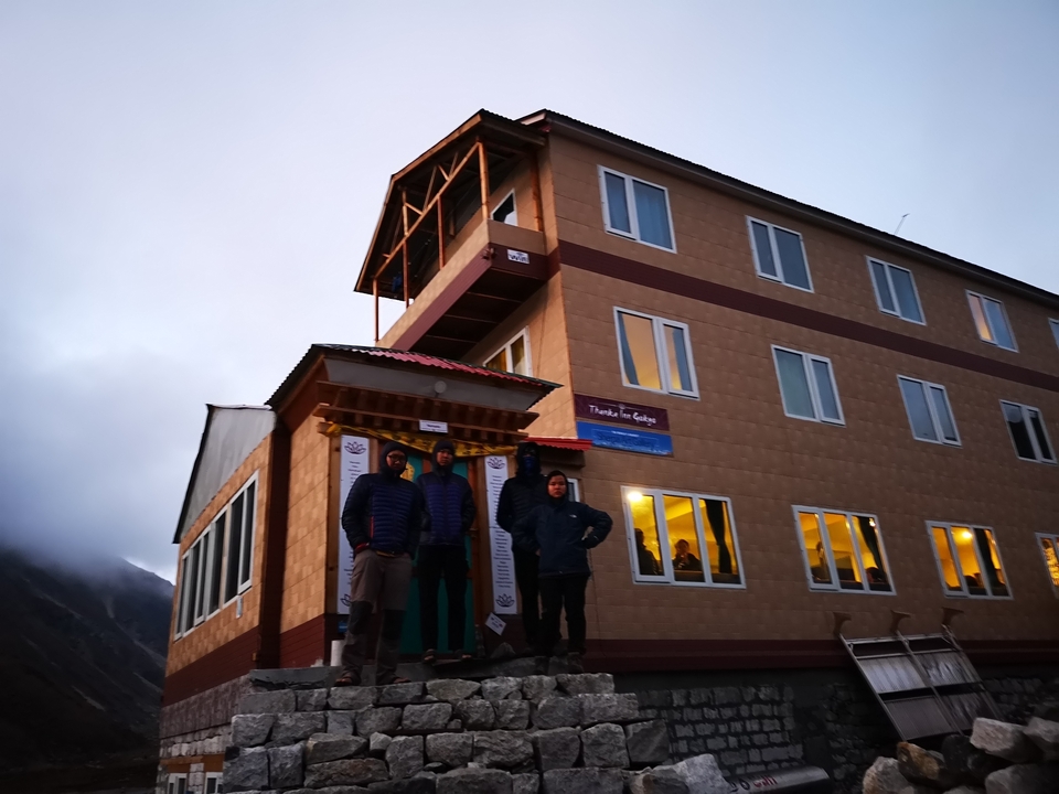 Trois personnes debout devant un bâtiment au crépuscule.