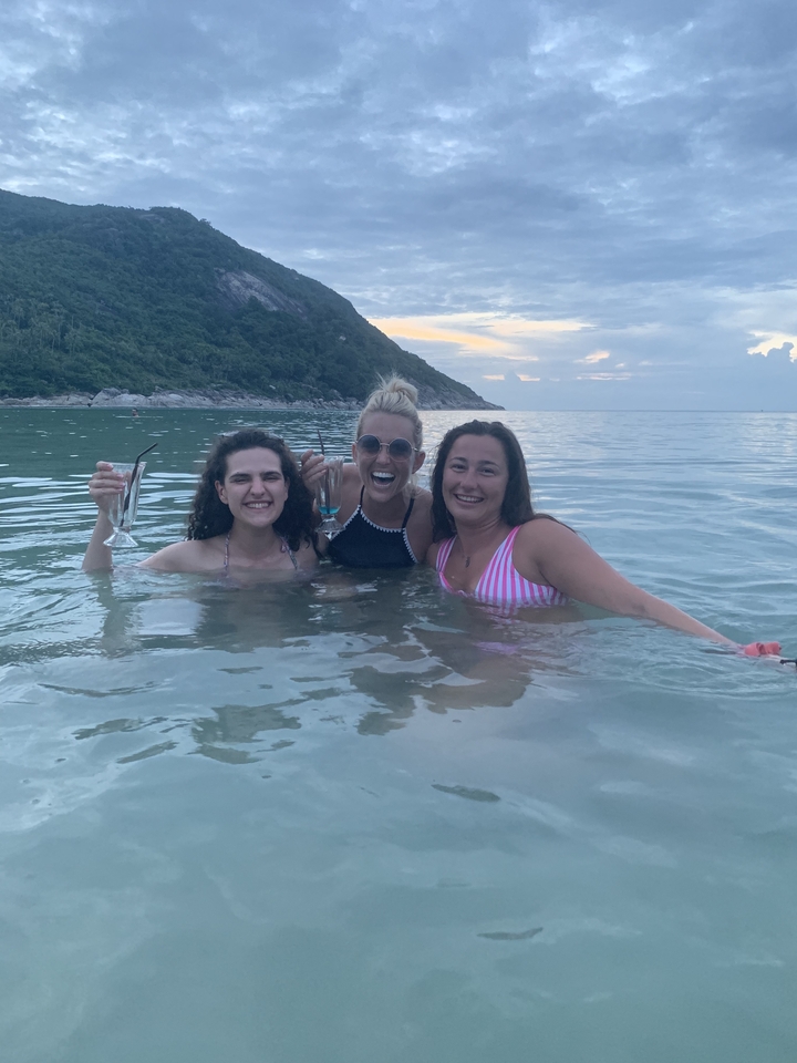 Three women drinking in the sea with a scenic view.
