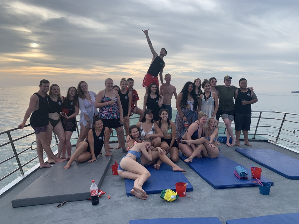 Large group of people on a boat posing for a photo during sunset.