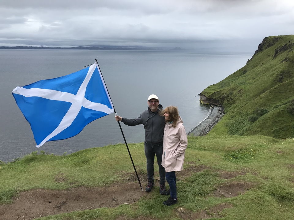 Couple holding a Scottish flag standing on a cliff overlooking the sea.