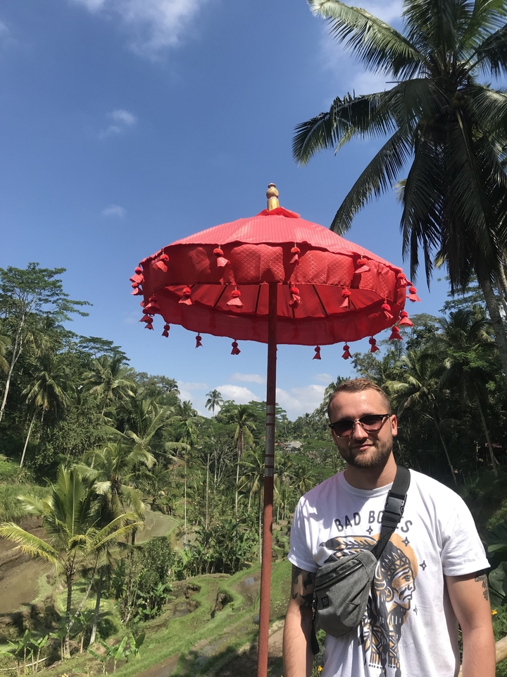 Man standing under a red umbrella against a tropical backdrop.