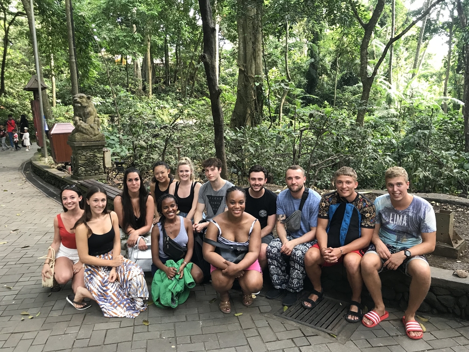 A large group of people posing outdoors in a forest area.
