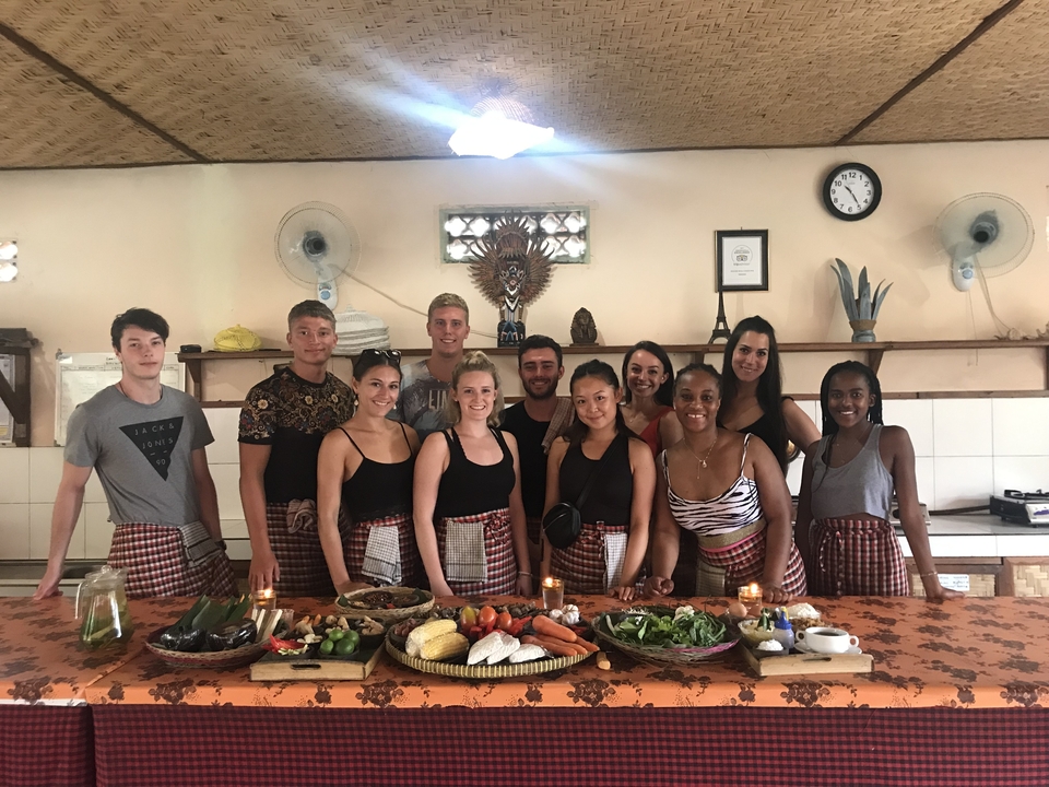 Group of people posing with a variety of food on a table.